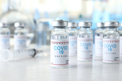 Photo of Glass vials with COVID-19 vaccine on white wooden table