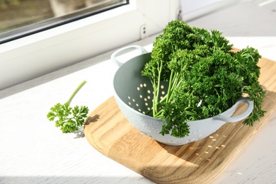 Photo of Colander with fresh green parsley on window sill indoors