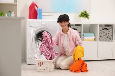 Photo of Happy woman with laundry near washing machine indoors