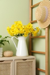 Jug with beautiful daffodils on table indoors