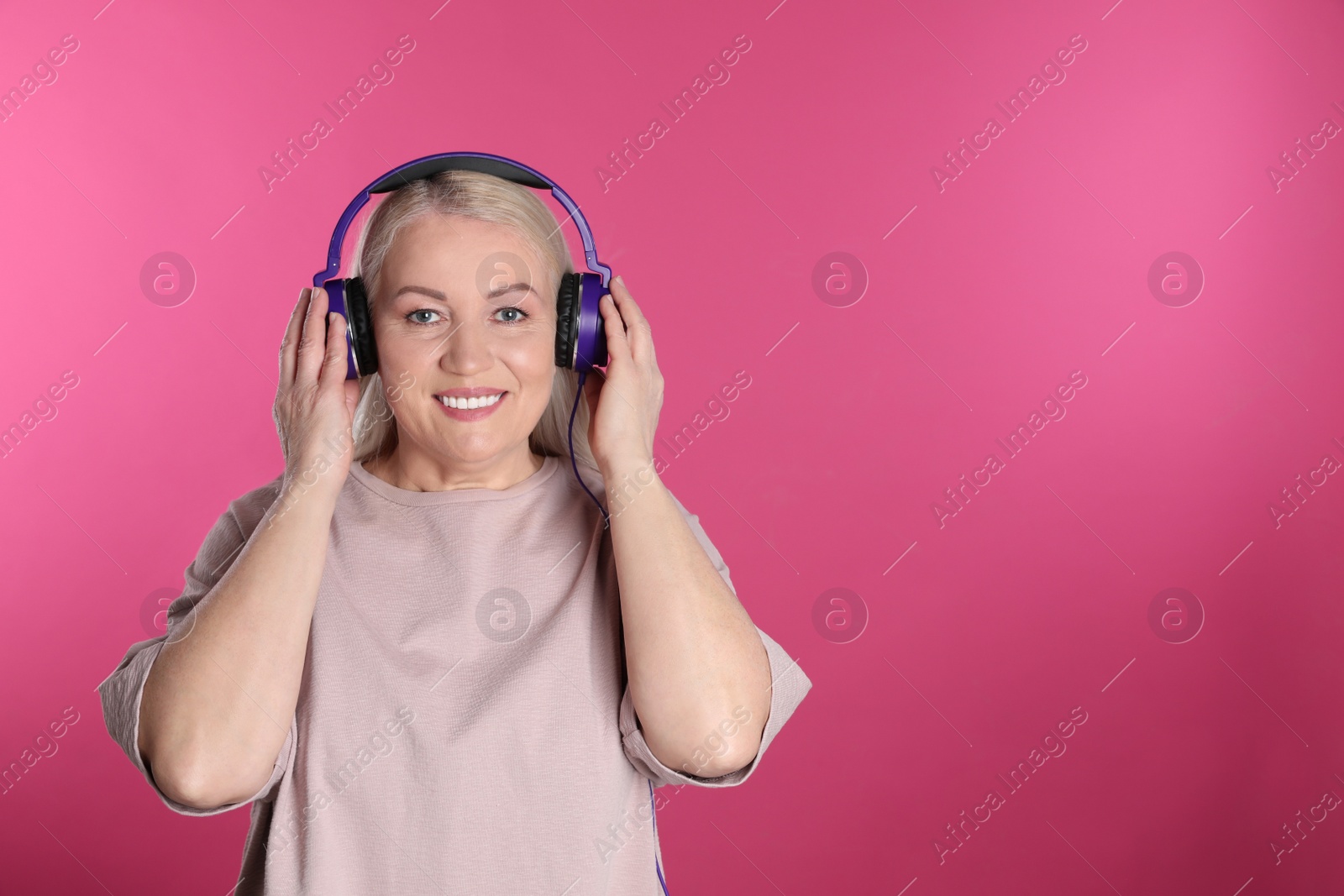 Photo of Mature woman enjoying music in headphones on color background. Space for text