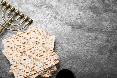 Photo of Stack of traditional matzos, menorah and red wine on grey table, flat lay. Space for text