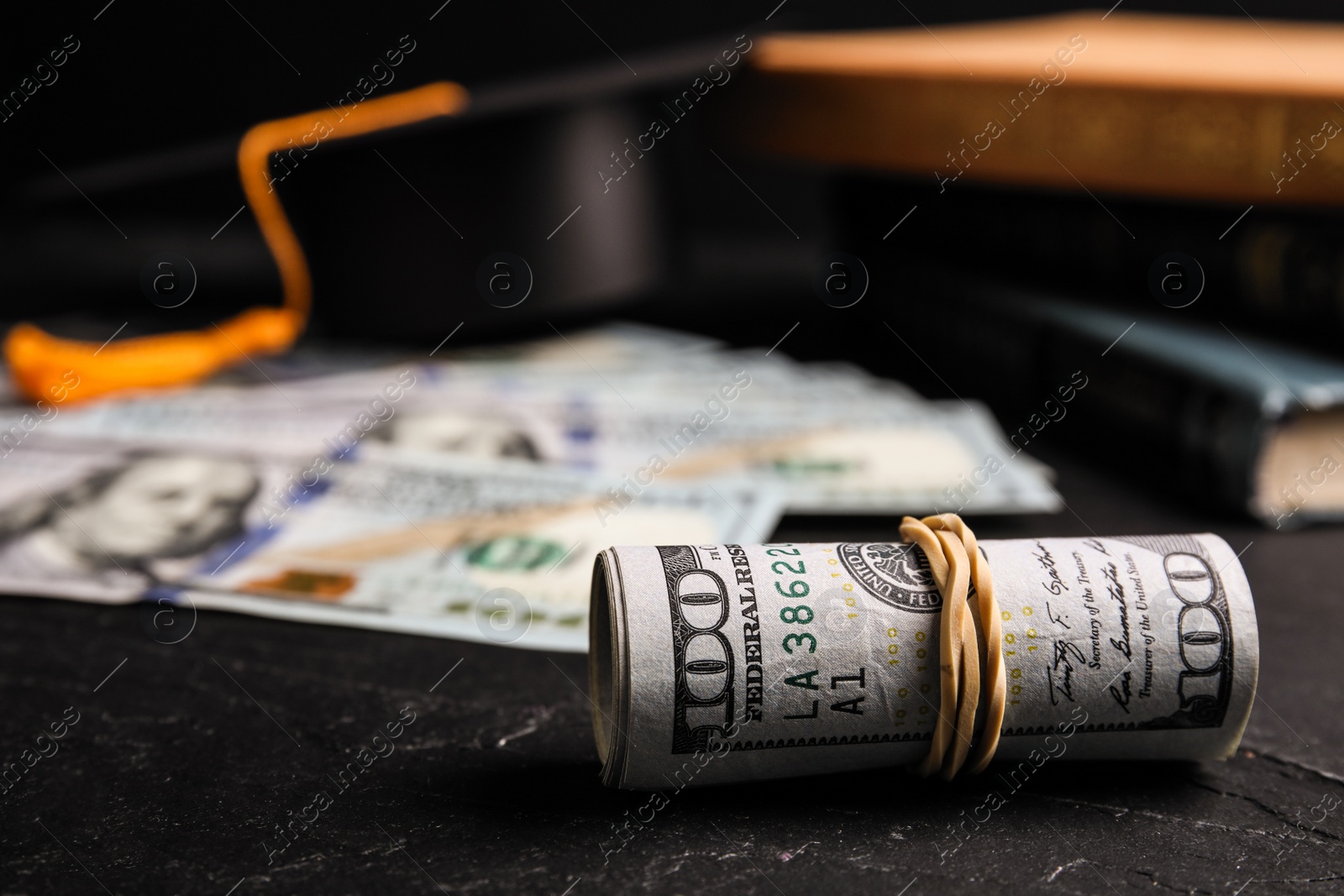 Photo of Dollar banknotes, student graduation hat and books on black table. Tuition fees concept