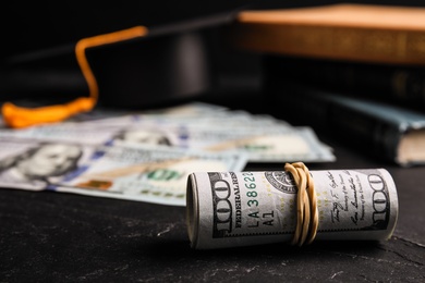 Photo of Dollar banknotes, student graduation hat and books on black table. Tuition fees concept