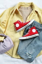 Photo of Pair of stylish red sneakers, clothes and bag on white fabric, flat lay