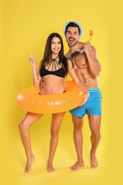 Photo of Young attractive couple in beachwear with snorkel and inflatable ring on yellow background