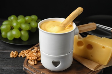 Pot of tasty cheese fondue and bread stick on black wooden table