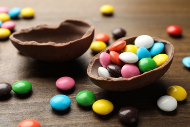 Photo of Broken chocolate egg and colorful candies on wooden table, closeup