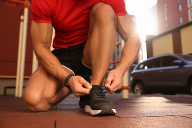 Photo of Man tying shoelaces before training at outdoor gym, closeup