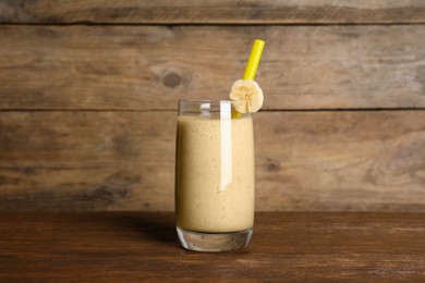 Photo of Glass of tasty smoothie with straw and cut banana piece on wooden table