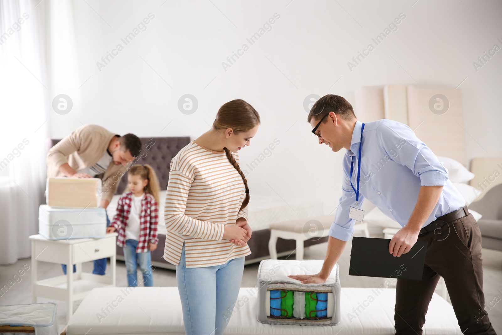 Photo of Salesman showing young woman section of mattress in store