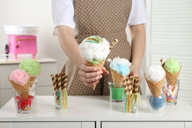 Photo of Woman holding waffle cone with cotton candy indoors, closeup