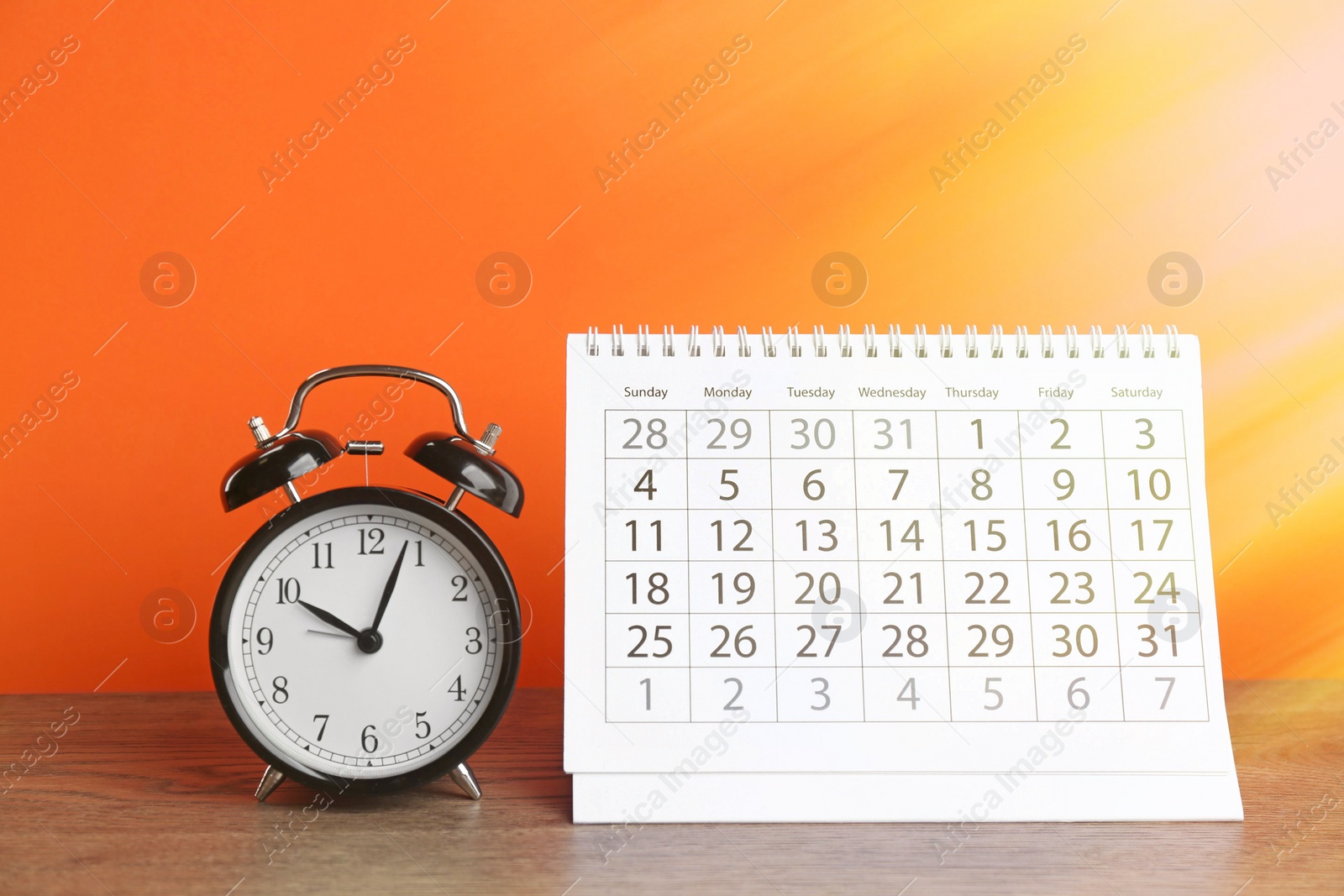 Image of Calendar and alarm clock on wooden table against orange background