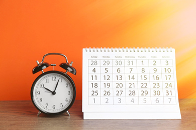 Image of Calendar and alarm clock on wooden table against orange background