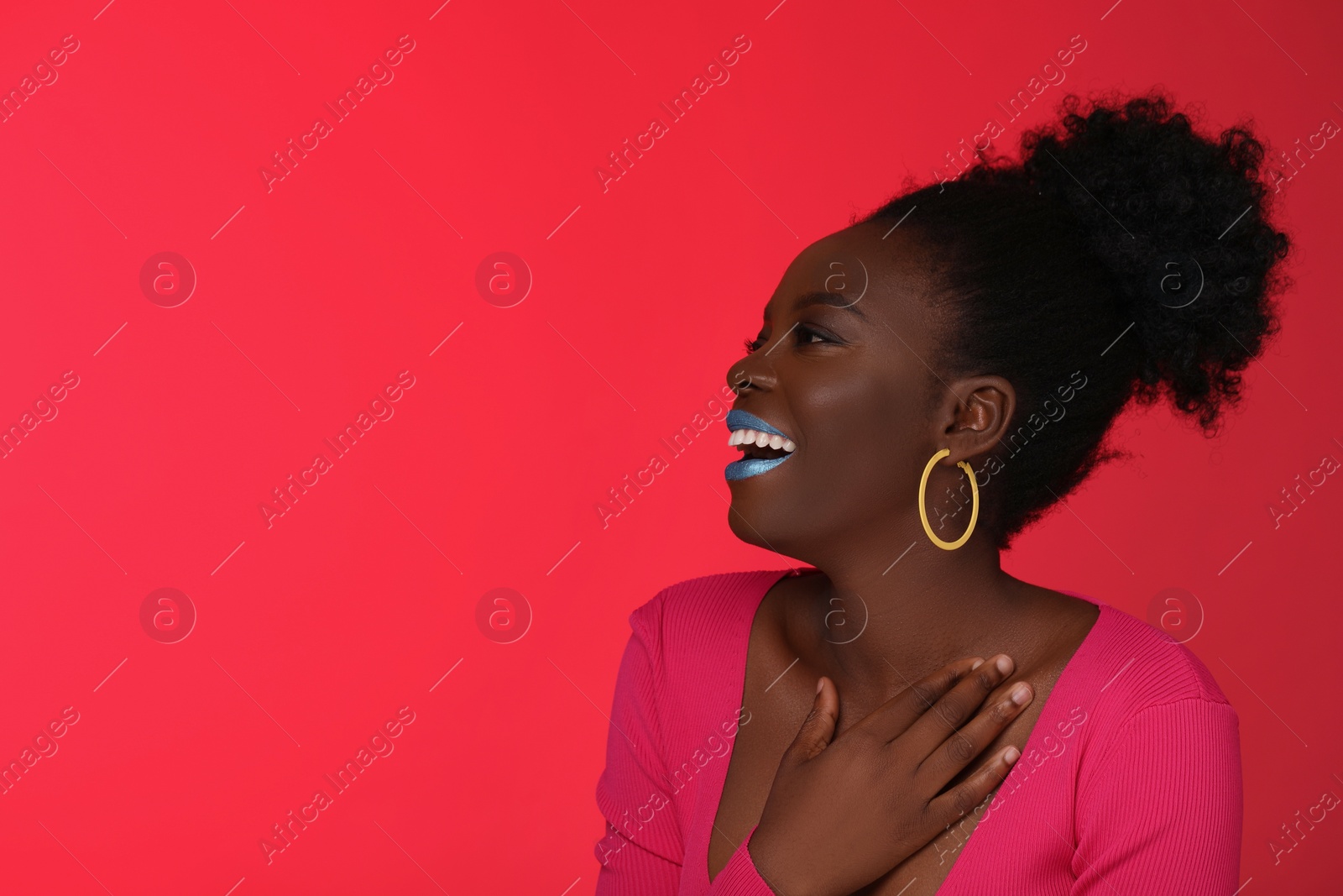Photo of Fashionable portrait of beautiful happy woman with bright makeup on coral background, space for text