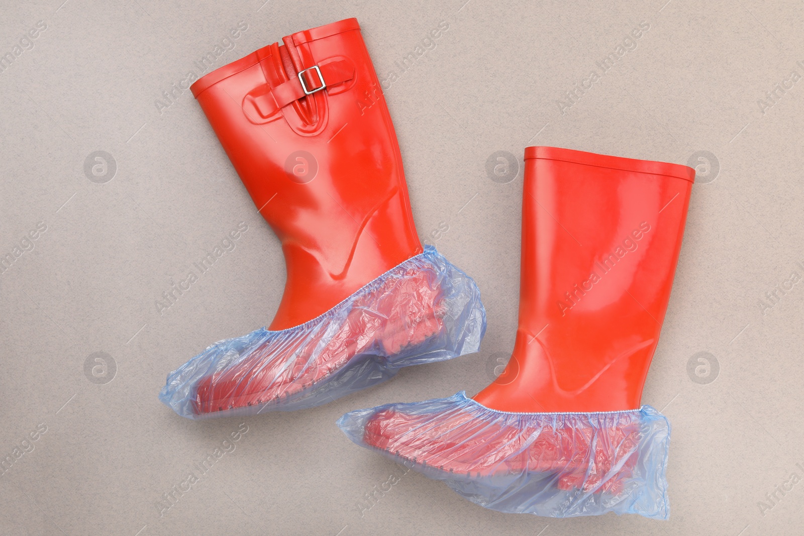 Photo of Rubber boots in shoe covers on grey background, top view