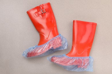 Photo of Rubber boots in shoe covers on grey background, top view