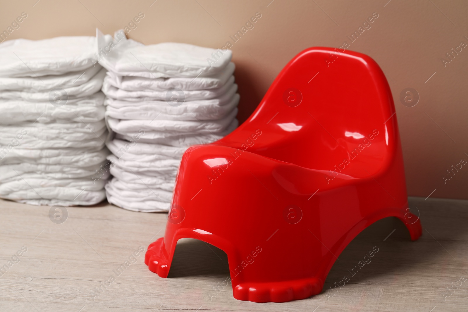 Photo of Red baby potty and diapers near brown wall. Toilet training