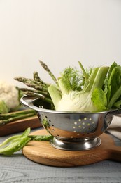 Metal colander with fennel, lettuce and asparagus on gray wooden table