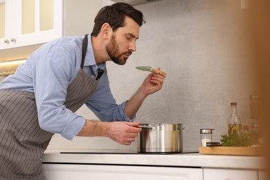 Man tasting delicious soup with spoon in kitchen