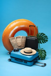 Photo of Suitcases, beach accessories and tropical leaves on light blue background. Summer vacation