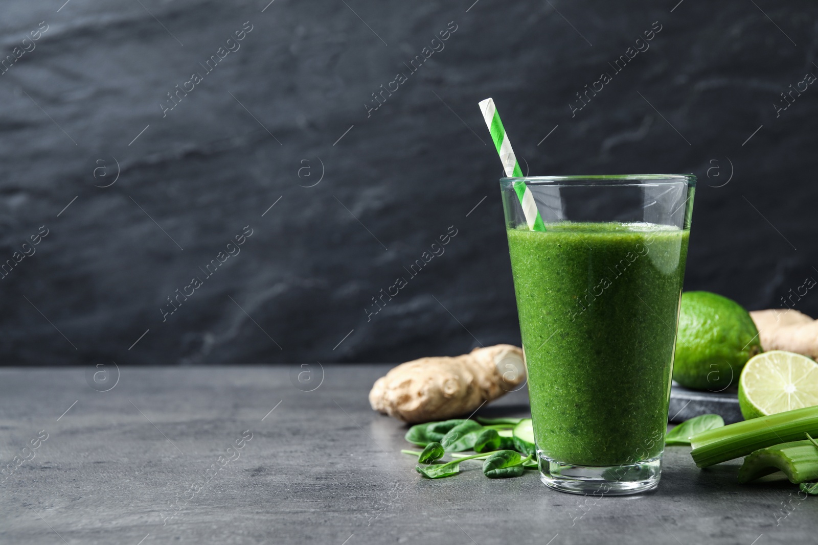 Photo of Green juice and fresh ingredients on grey table. Space for text