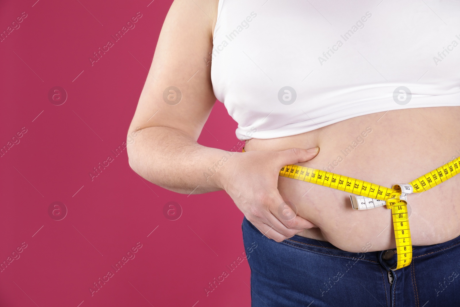 Photo of Overweight woman measuring waist with tape on color background, closeup. Space for text