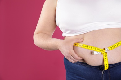 Overweight woman measuring waist with tape on color background, closeup. Space for text