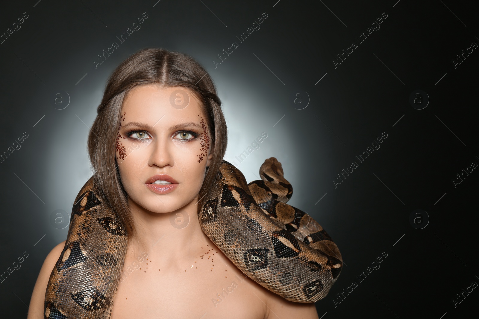 Photo of Beautiful woman with boa constrictor on dark background. Space for text