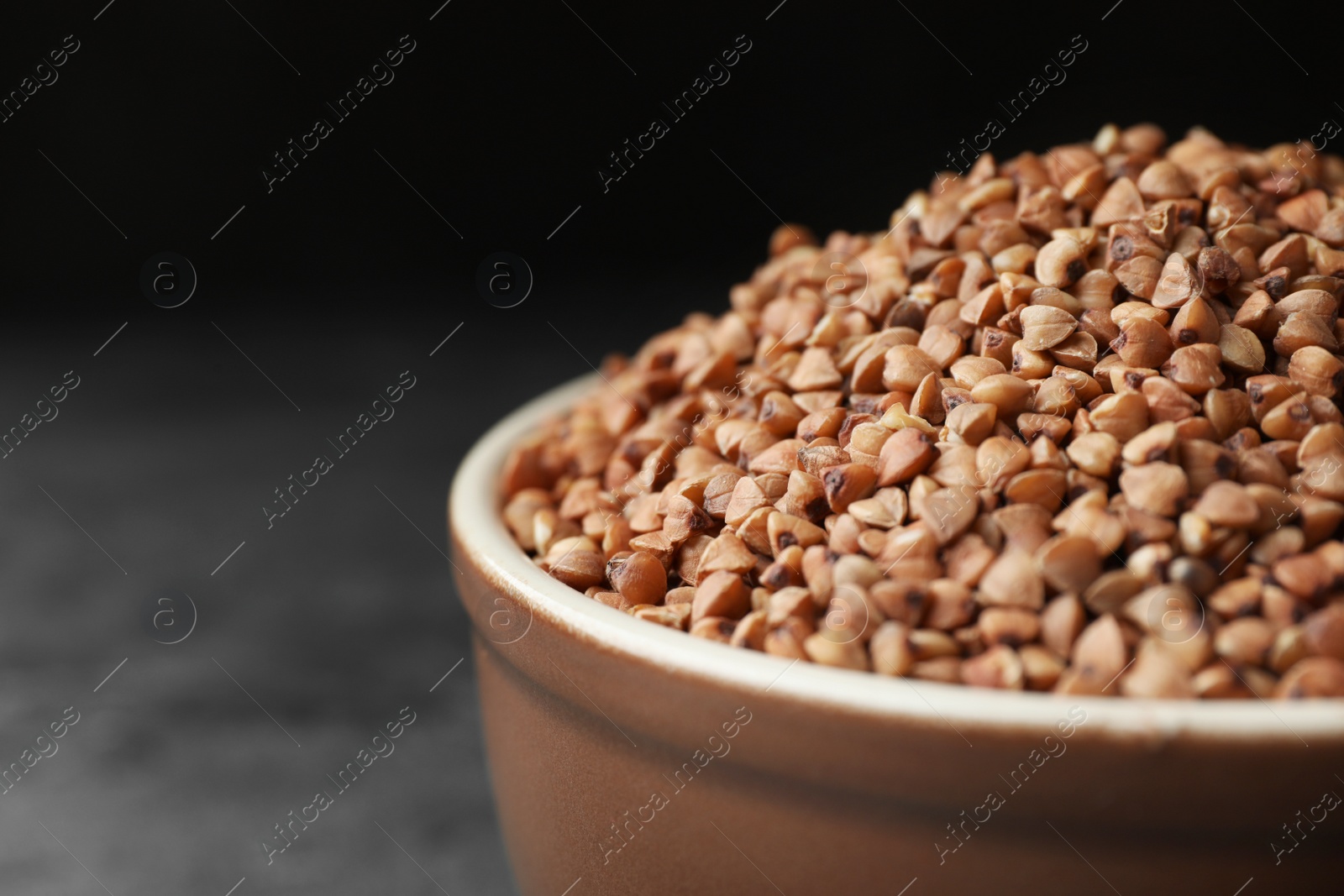 Photo of Uncooked buckwheat grains on grey table, closeup