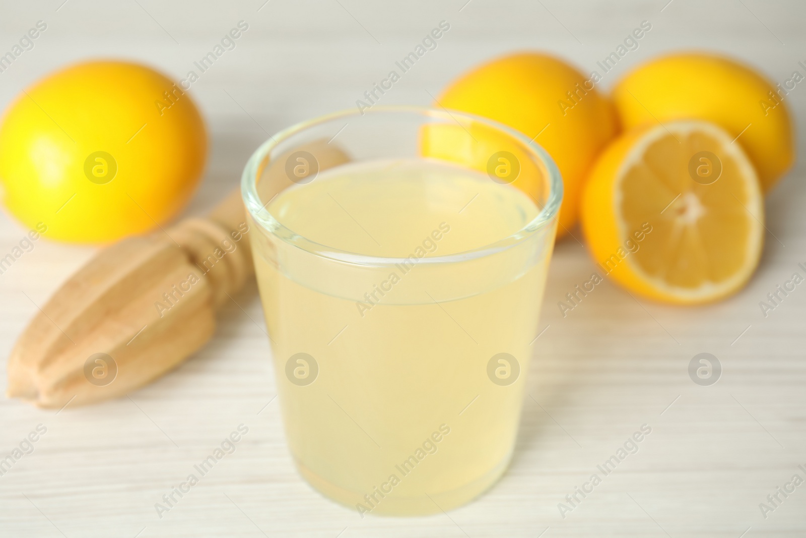 Photo of Freshly squeezed juice, lemons and reamer on white wooden table