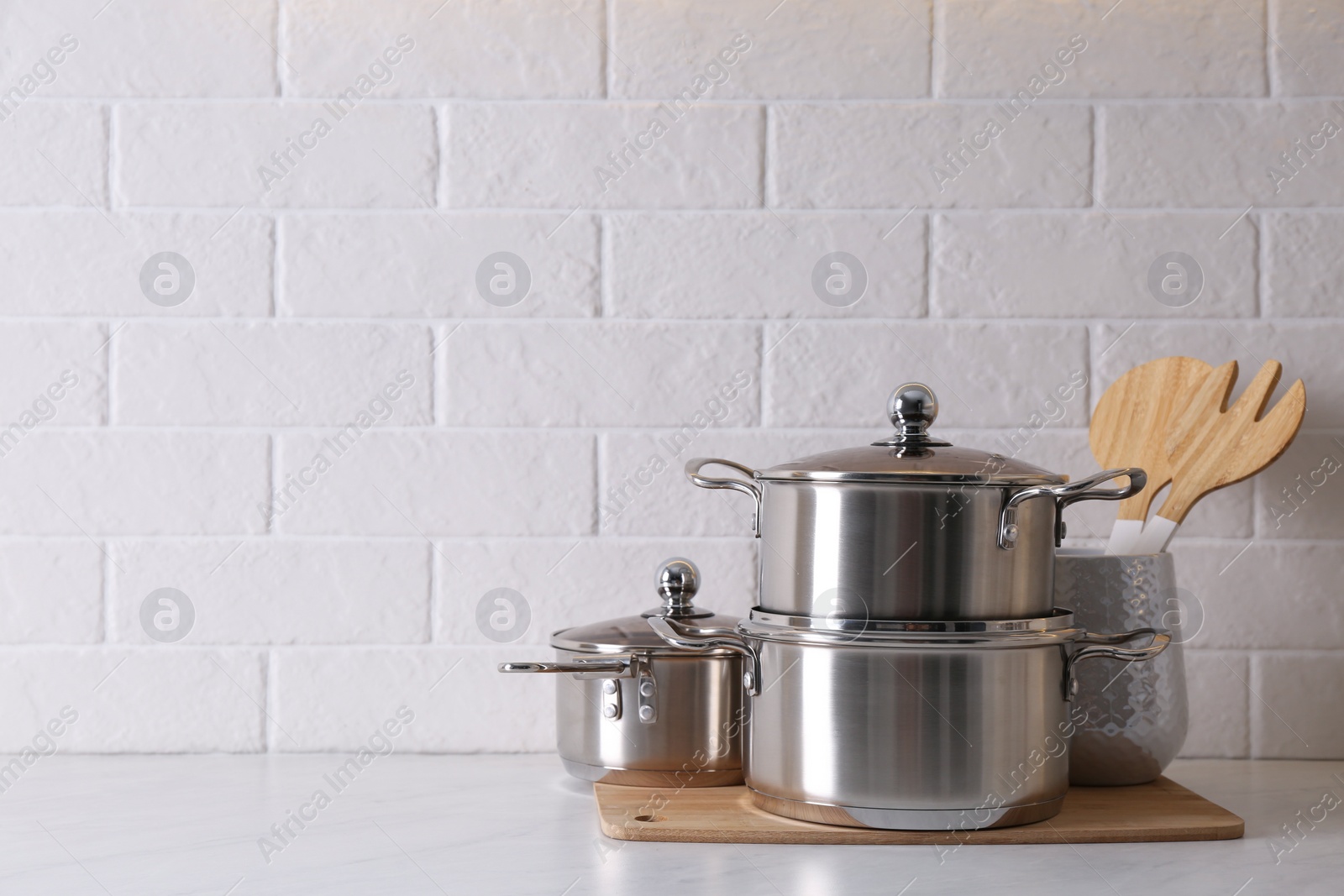 Photo of Set of stainless steel cookware and kitchen utensils on table near white brick wall, space for text