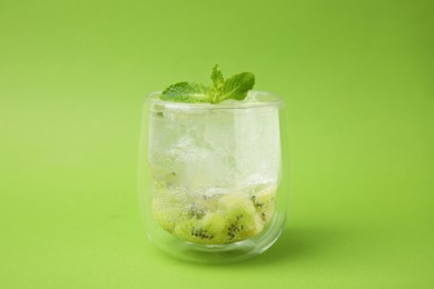 Glass of refreshing drink with kiwi and mint on light green background