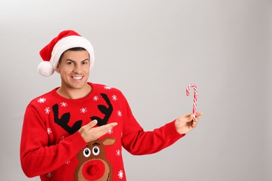 Handsome man in Santa hat holding candy cane on grey background