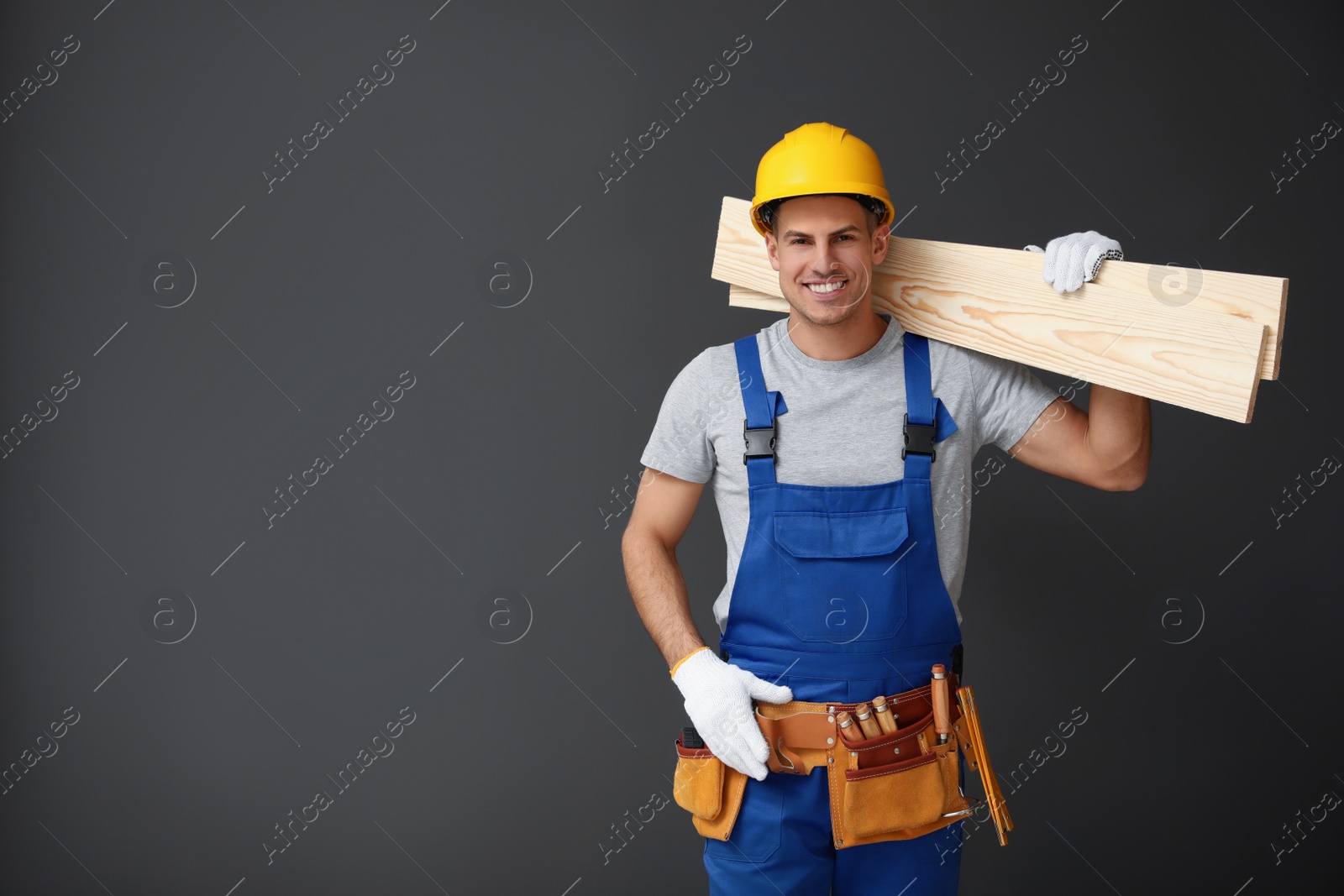 Photo of Handsome carpenter with wooden planks on dark background. Space for text