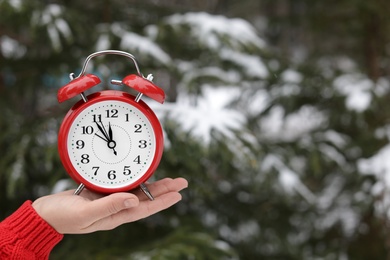 Photo of Woman holding red alarm clock near fir tree covered with snow outdoors. Space for text