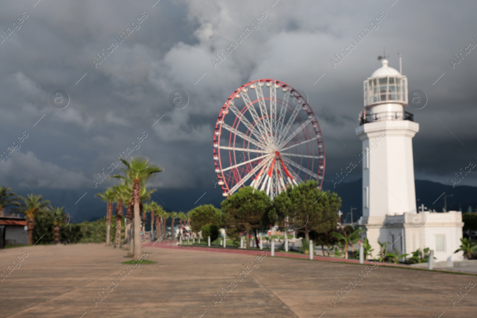 Photo of Blurred view of large Ferris wheel and lighthouse under rainy clouds
