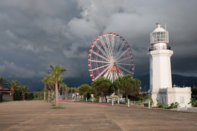 Blurred view of large Ferris wheel and lighthouse under rainy clouds