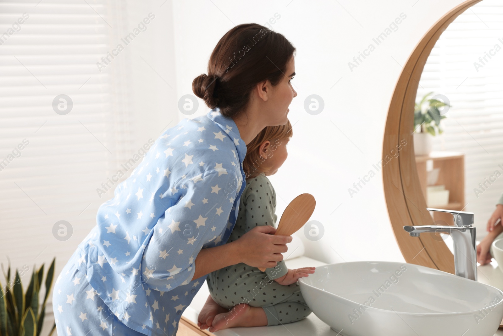 Photo of Mother brushing hair of her little daughter in bathroom
