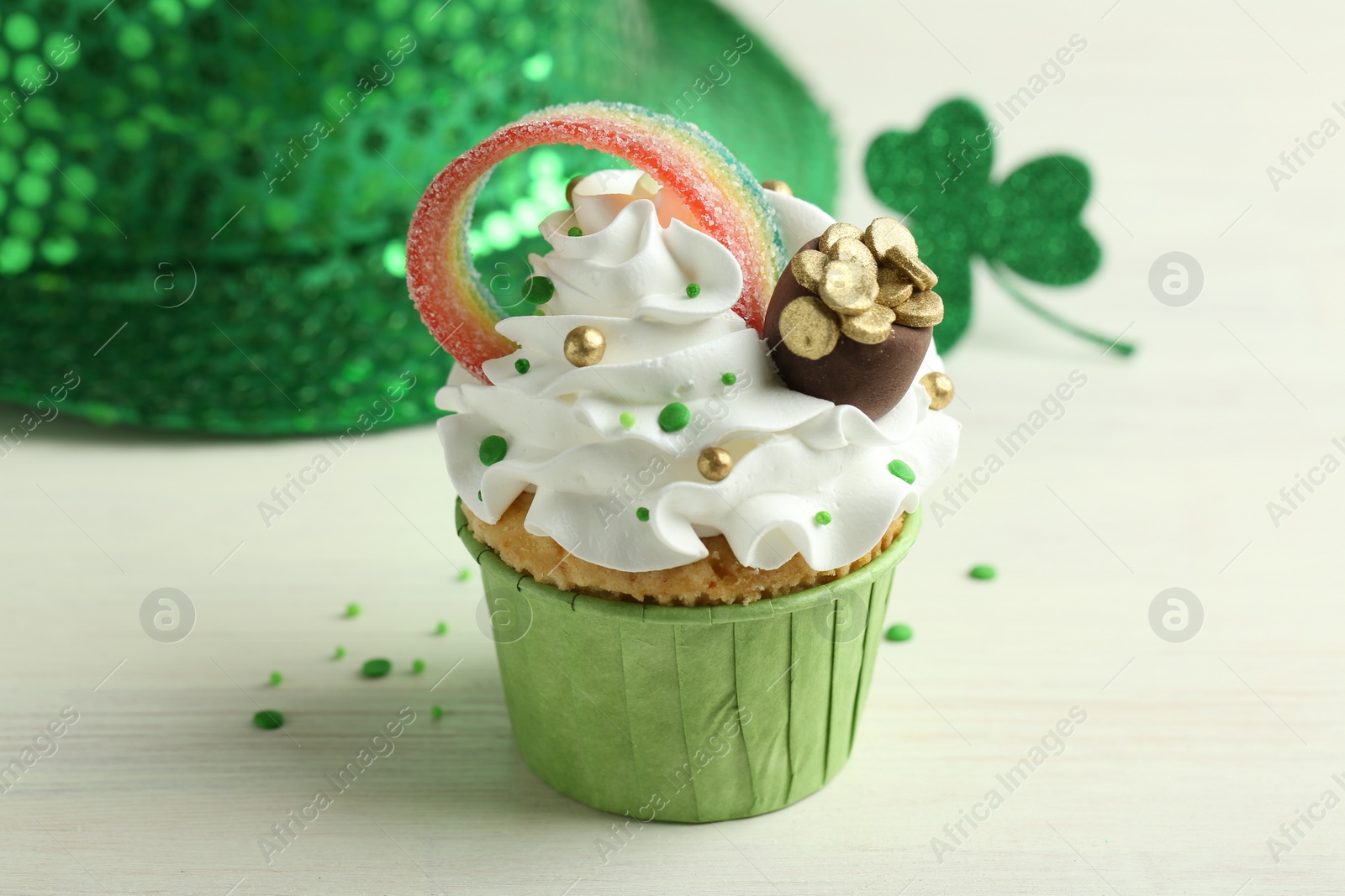 Photo of St. Patrick's day party. Tasty cupcake with sour rainbow belt and pot of gold toppers on white table, closeup