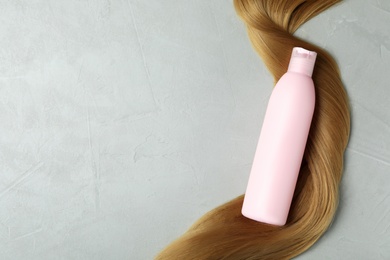 Blank bottle of cosmetic product and hair on light background, flat lay. Space for design