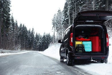 Photo of Car with open trunk full of luggage near snowy road in forest