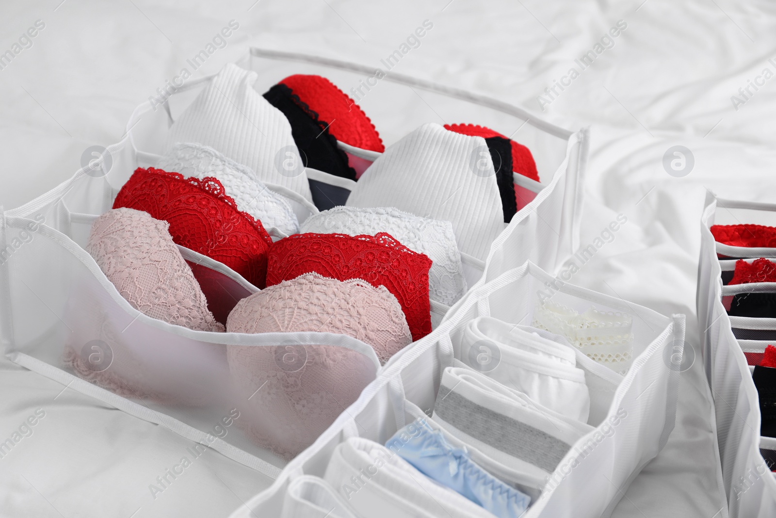 Photo of Organizers with stylish women's underwear on bed, closeup