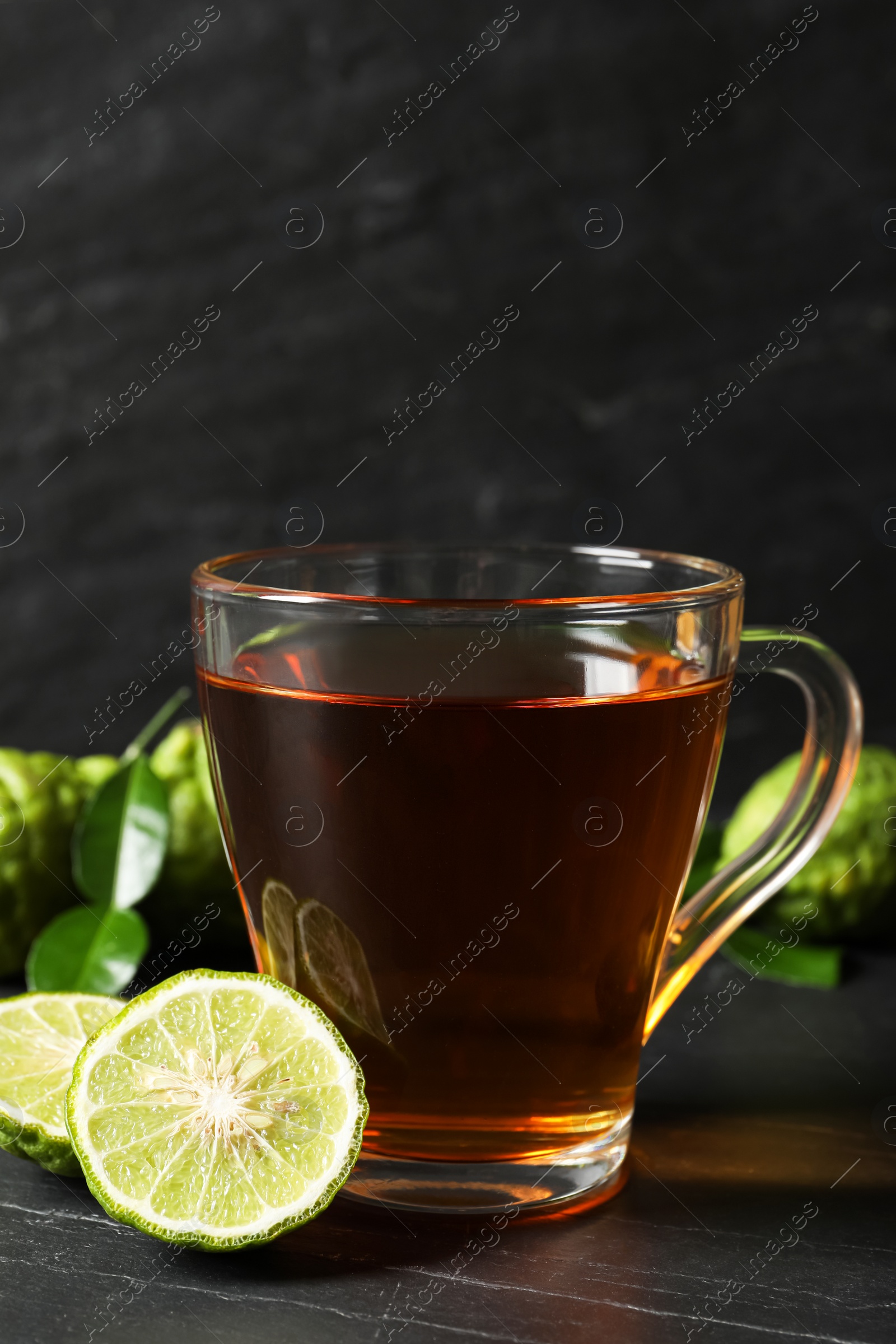 Photo of Glass cup of tasty bergamot tea and fresh fruits on black table