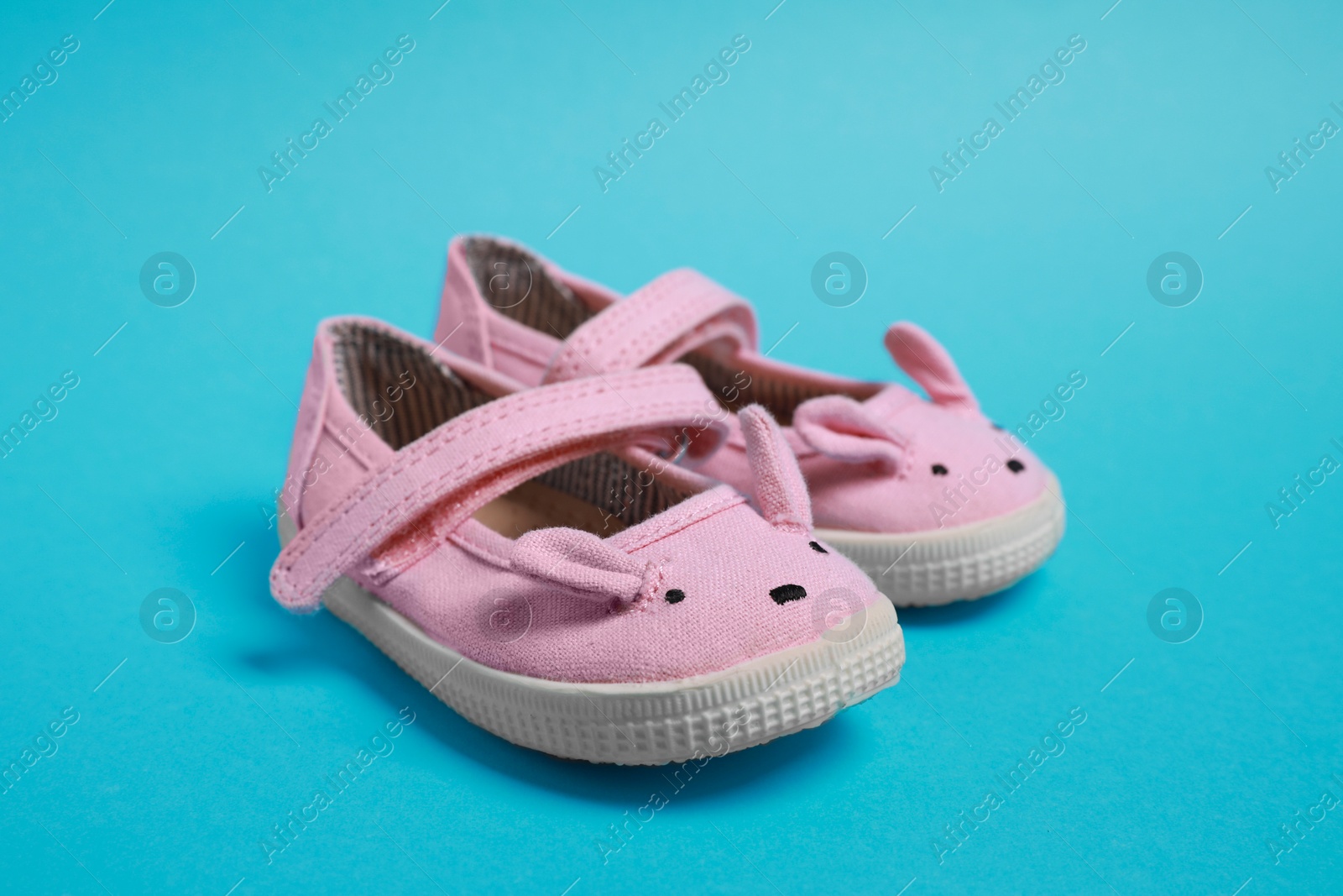 Photo of Pair of cute baby shoes on light blue background