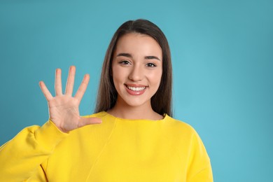 Photo of Woman showing number five with her hand on light blue background