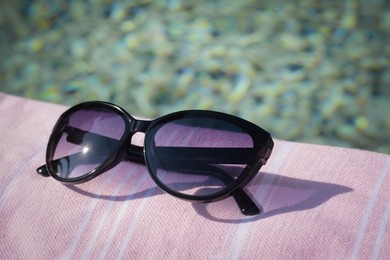 Photo of Stylish sunglasses on blanket near outdoor swimming pool, closeup
