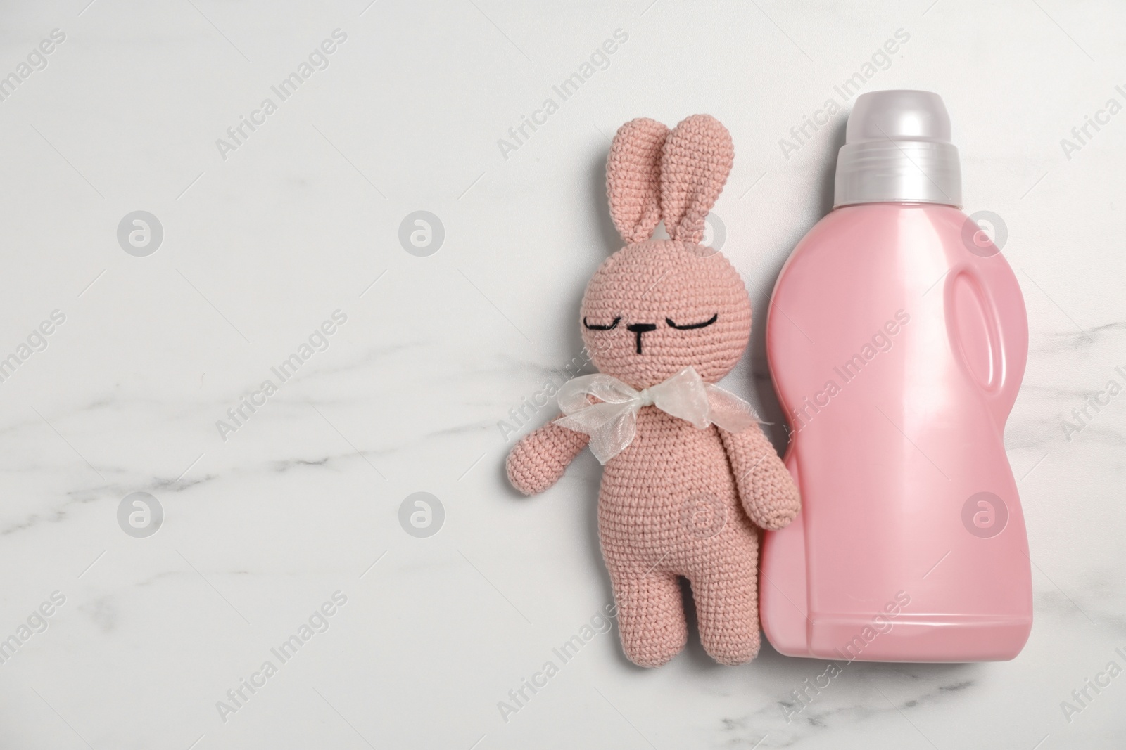 Photo of Bottle of laundry detergent and rabbit toy on white marble table, flat lay. Space for text