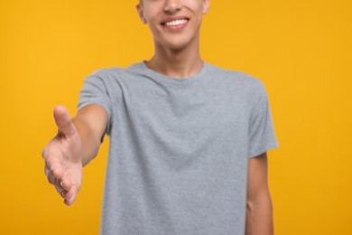 Photo of Happy man welcoming and offering handshake on orange background, selective focus