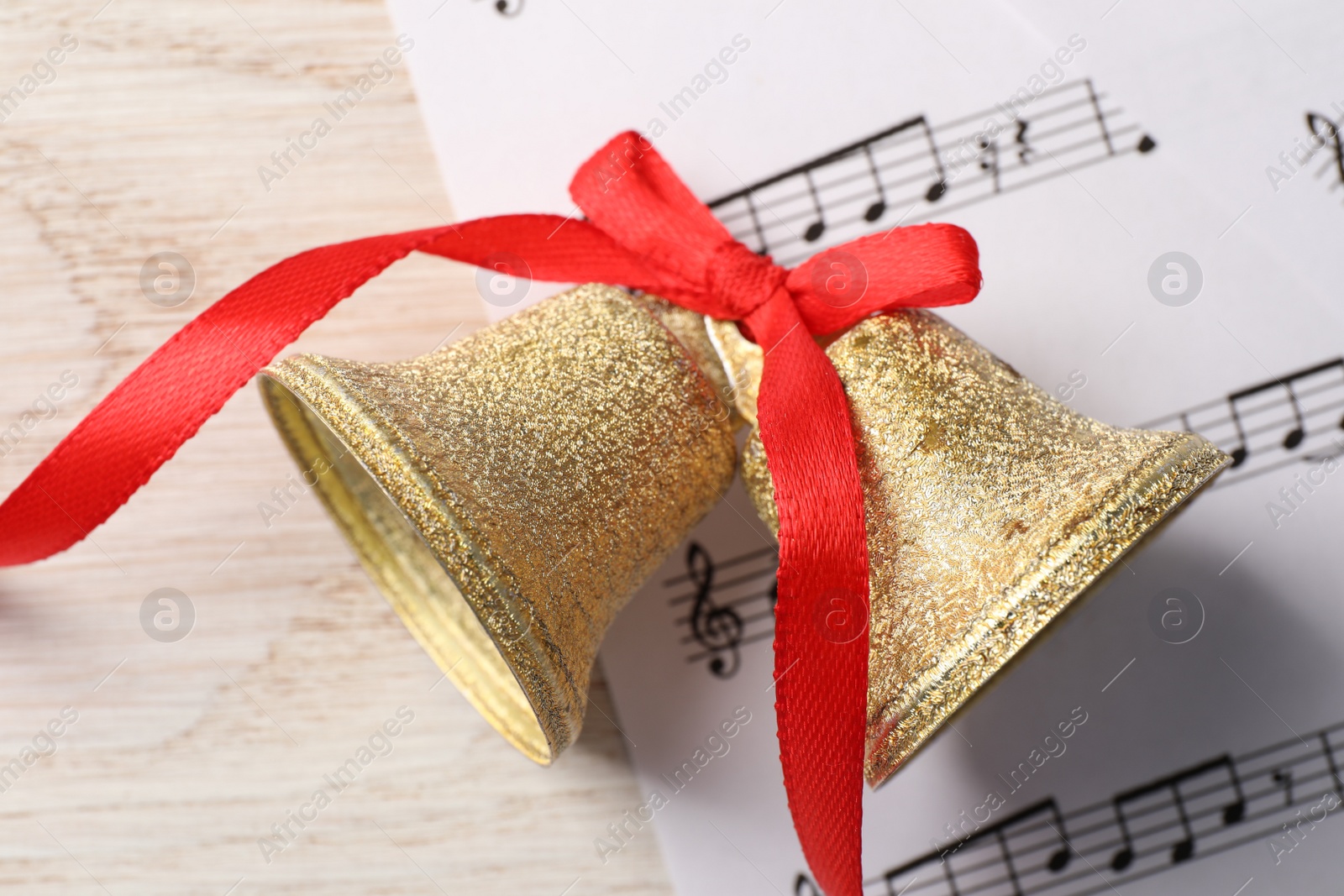 Photo of Golden shiny bells with red bow and music sheet on wooden table, top view. Christmas decoration